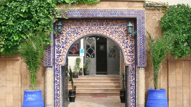 A hotel entrance with a decorative archway, steps leading up to the door, and potted plants on either side. - Al Jasira Hotel (Essaouira)