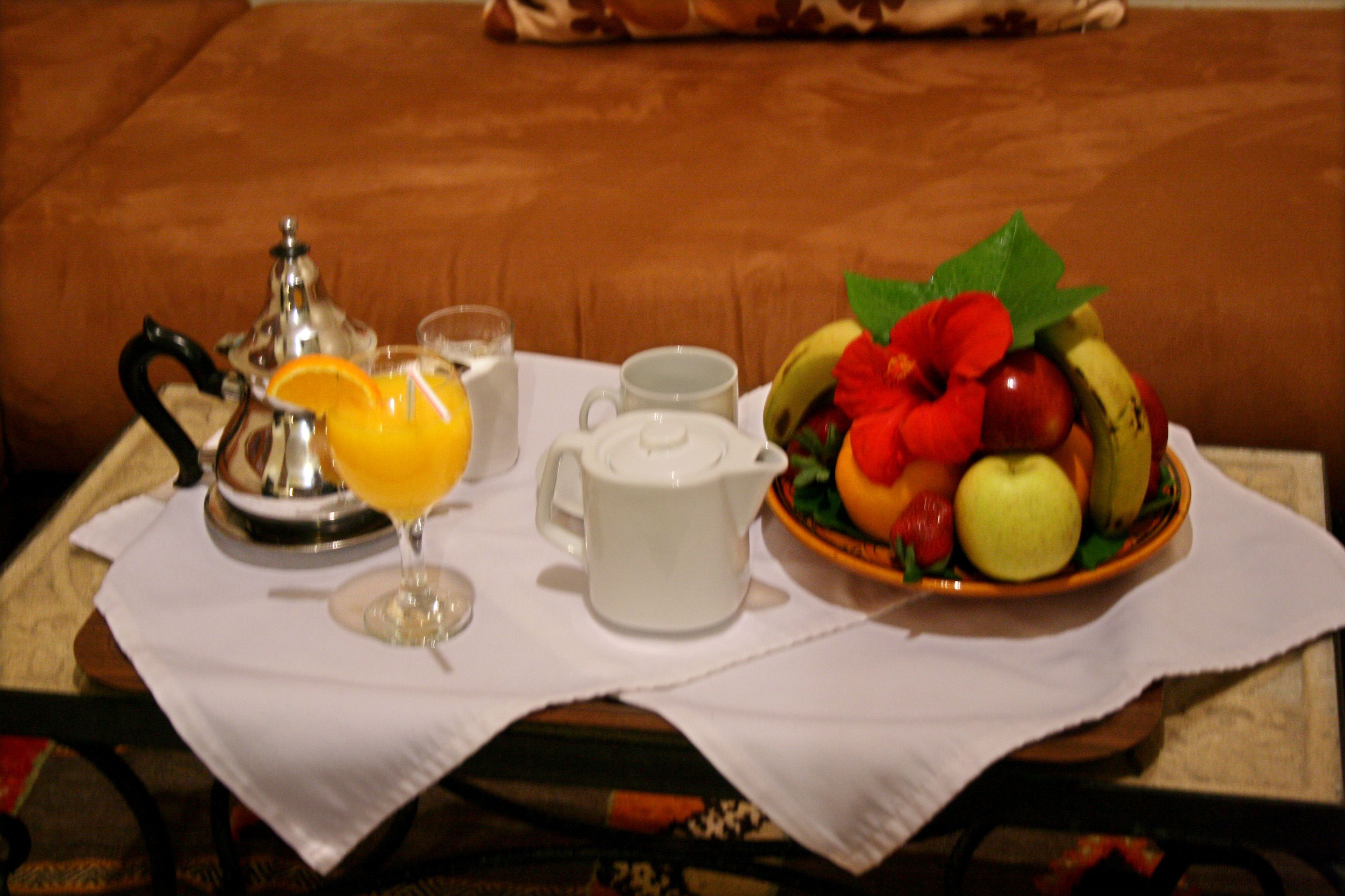 Una mesa con un servicio de desayuno que incluye un frutero, una tetera, una taza y un vaso de jugo de naranja.