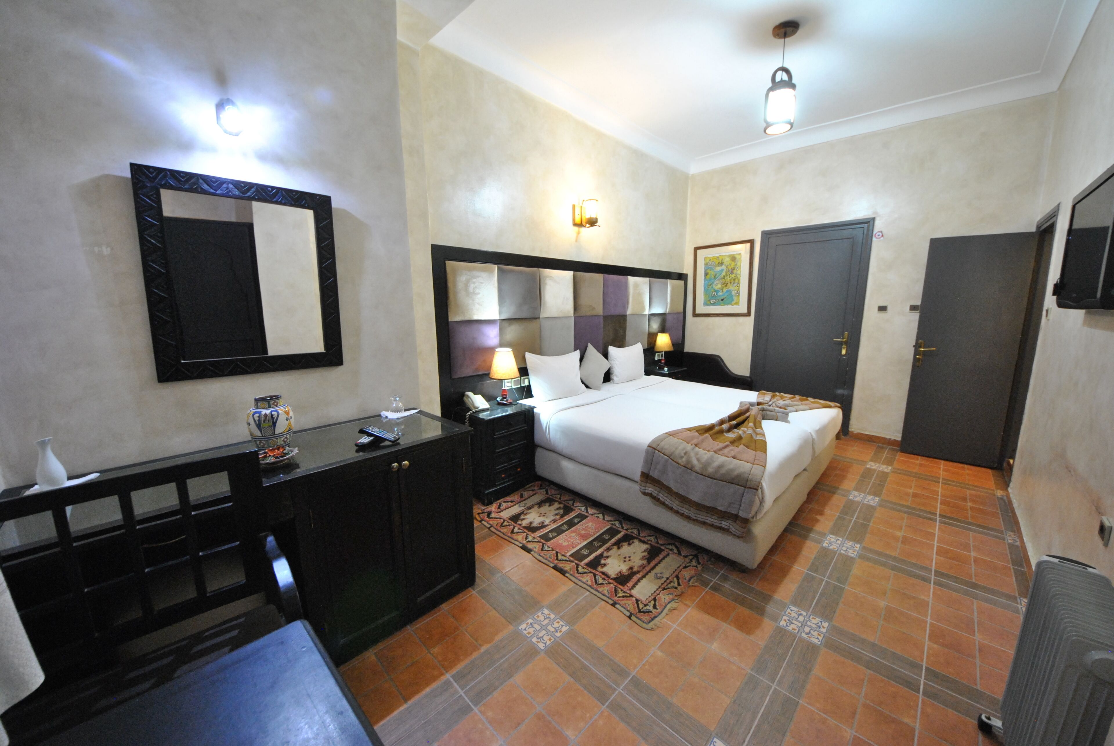 A hotel room with a bed, bedside table, lamp, and a large mirror.