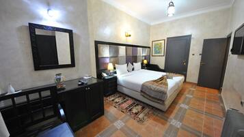 A hotel room with a bed, bedside table, lamp, and a large mirror.