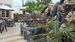 A patio area with outdoor seating, a stone wall with plant life, and a staircase leading to an upper level. - Al Jasira Hotel (Essaouira)