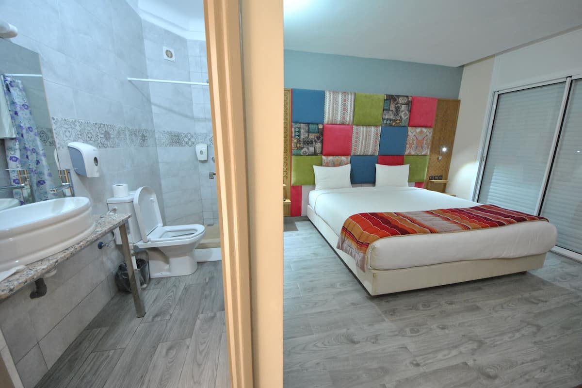 Un baño con lavabo, inodoro y ducha, y un dormitorio con cama, cabecero colorido y ventana.