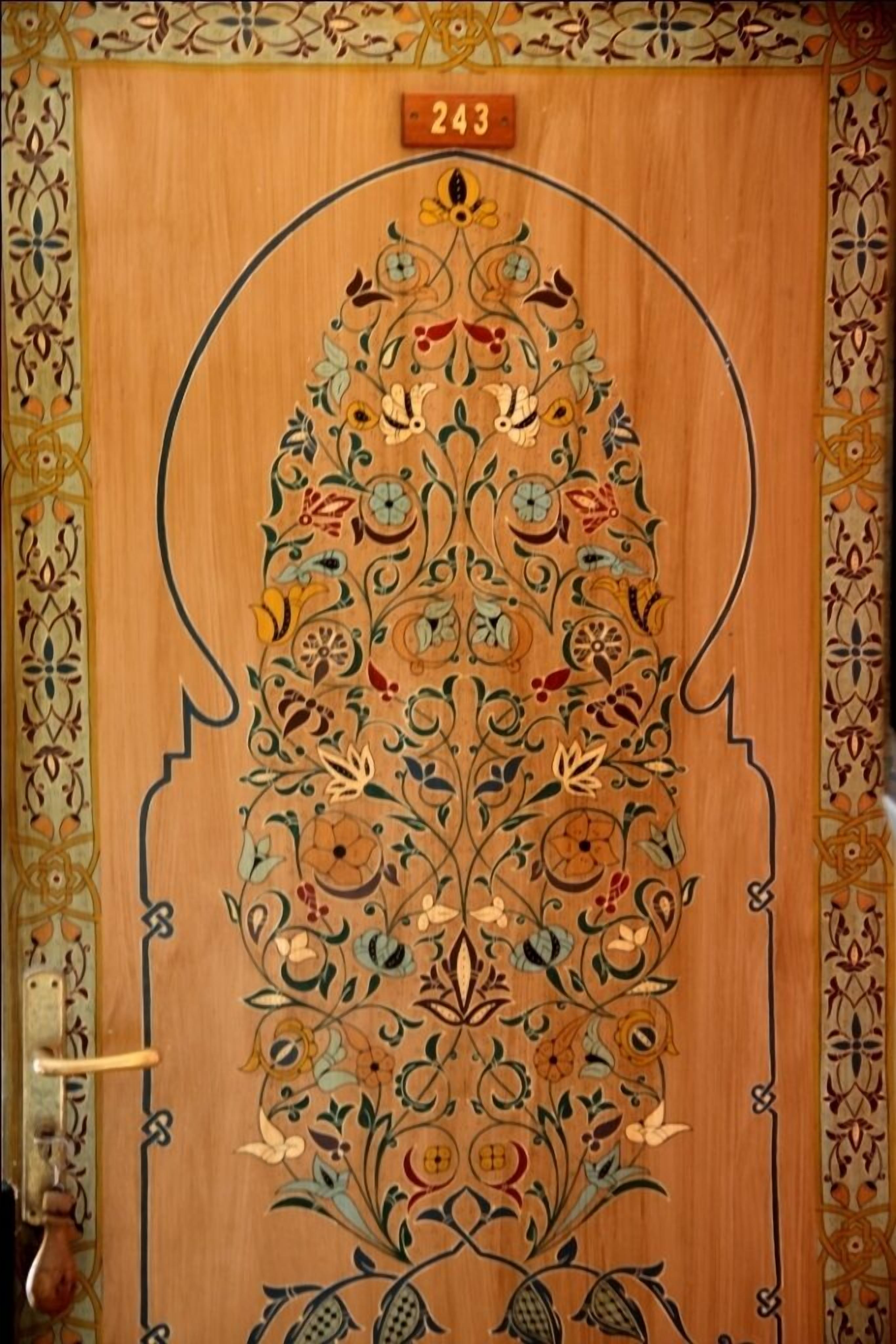 A wooden door with intricate floral and geometric patterns, a number '243' above it, and a handle on the left.