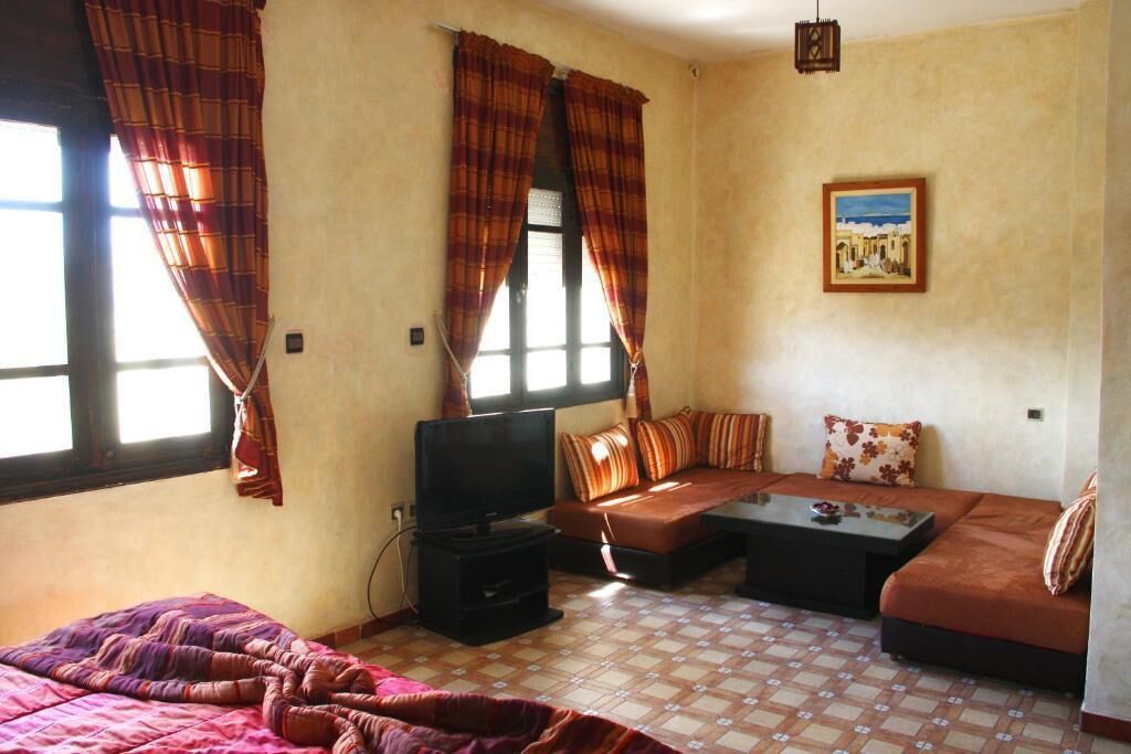 Una habitación con cama, sofá, televisión y ventana con cortinas.