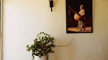 Un mur orné d’un tableau encadré représentant une personne jouant d’un instrument à cordes, d’une plante en pot et d’un luminaire fixé au mur.