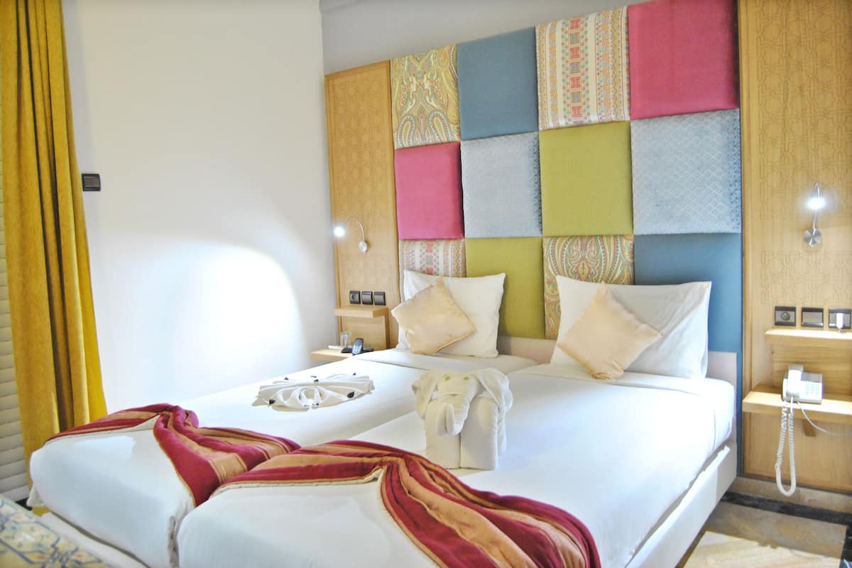 Una cama doble con cabecera de varios paneles estampados, una mesita de noche con lámpara y un teléfono.