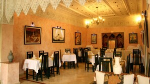 A dining area with tables and chairs, ornate ceiling, and framed artwork on the walls. - Al Jasira Hotel (Essaouira)