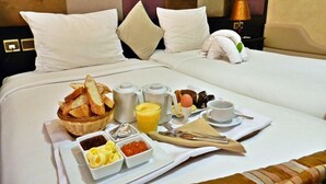 A neatly made bed with white linens, a basket of bread, condiments, and a breakfast tray including eggs, toast, and beverages. - Al Jasira Hotel (Essaouira)
