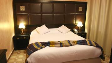 Habitación de hotel con una cama grande, dos mesitas de noche con lámparas y un cabecero con panel decorativo.