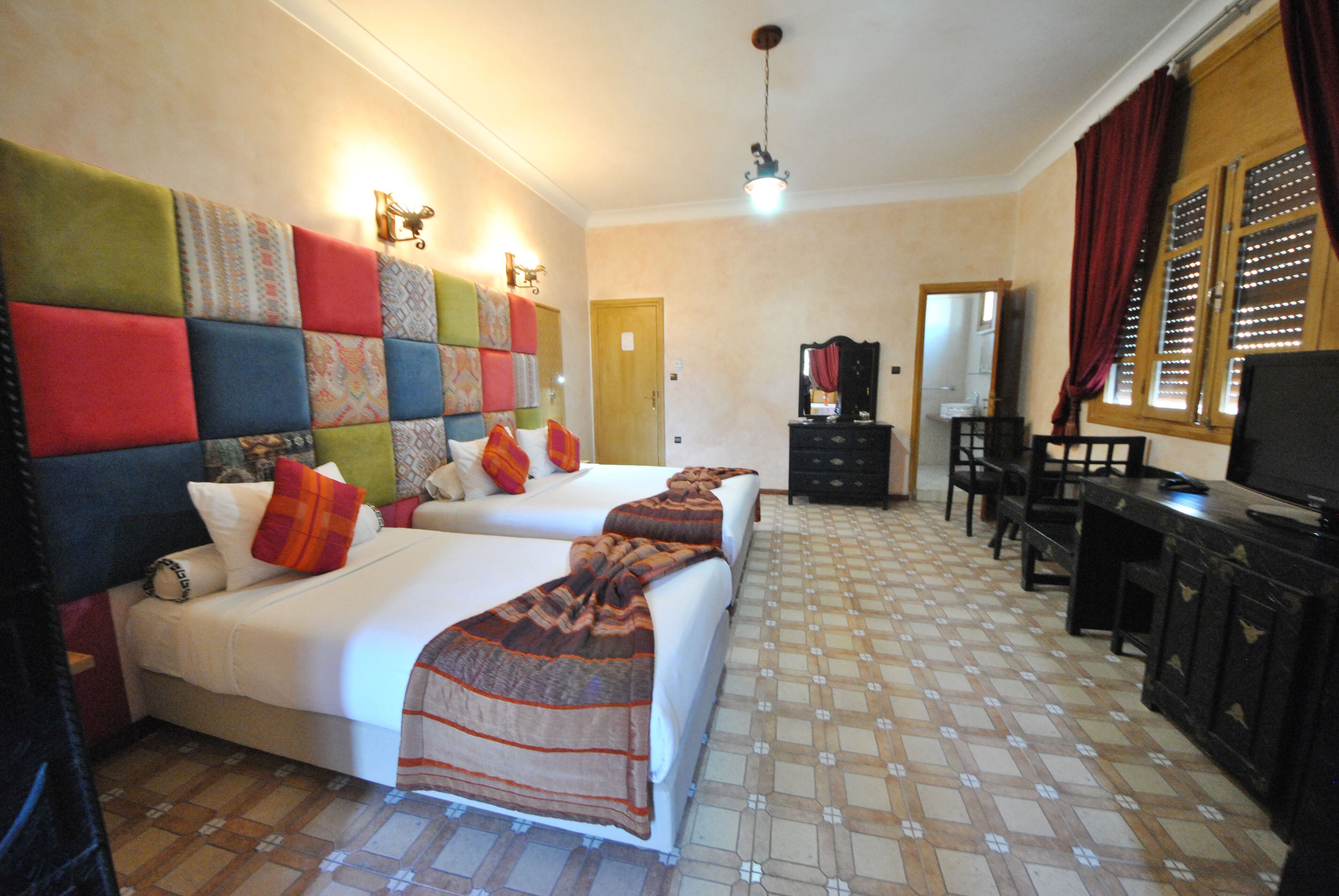 Habitación de hotel con dos camas, televisión, escritorio y espejo.