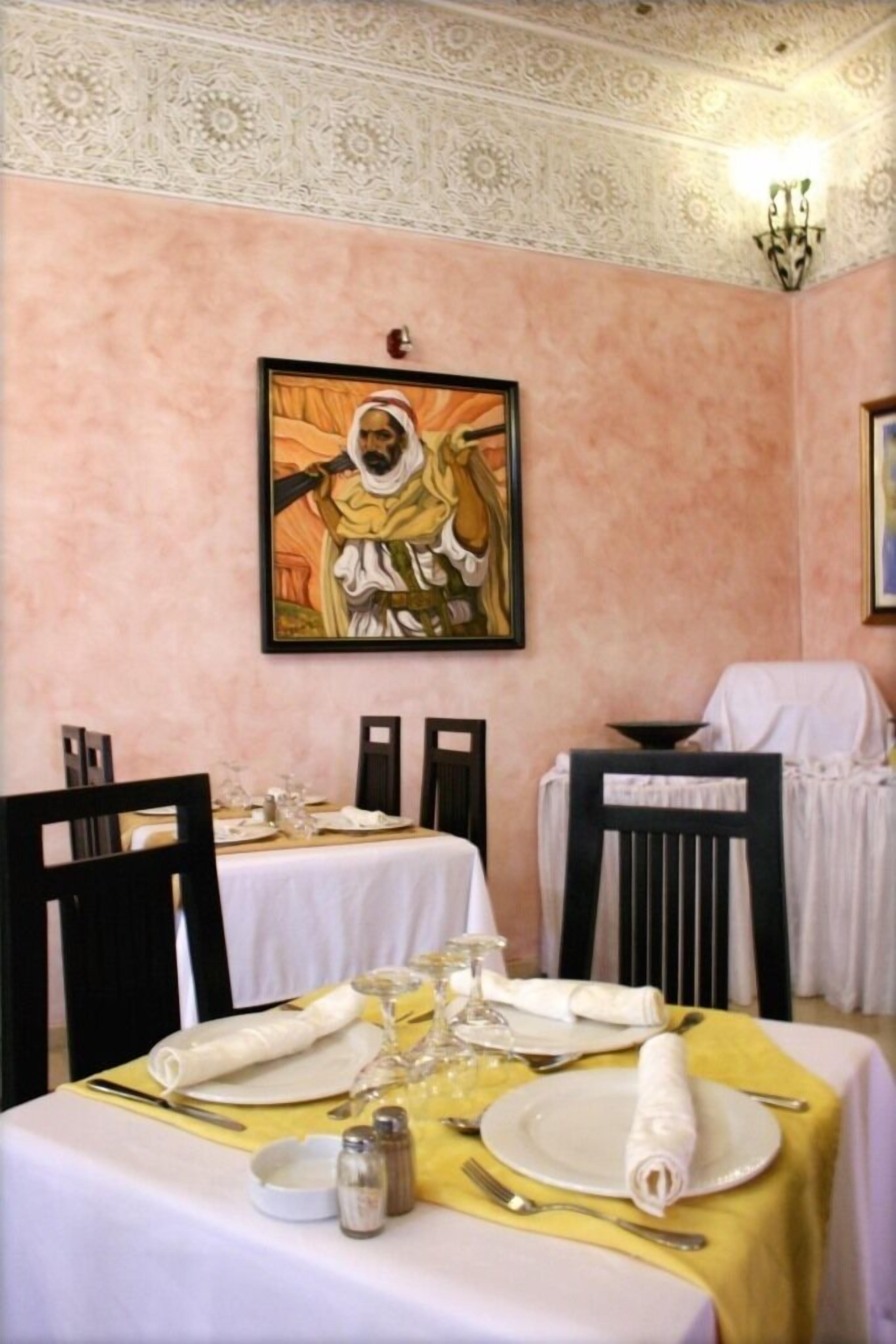 A dining area with two tables set for a meal, a painting on the wall, and a decorative ceiling.