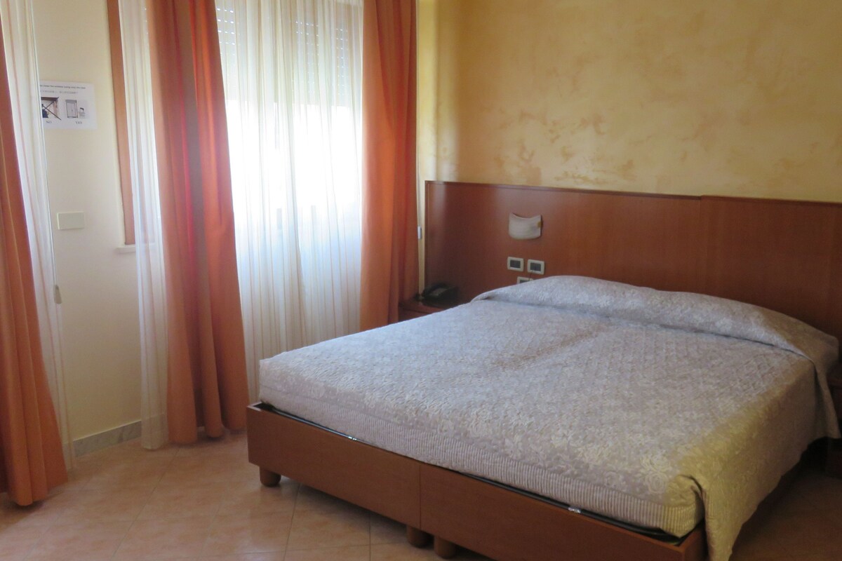 A room with a single bed, a wooden headboard, a nightstand, and a window with curtains.