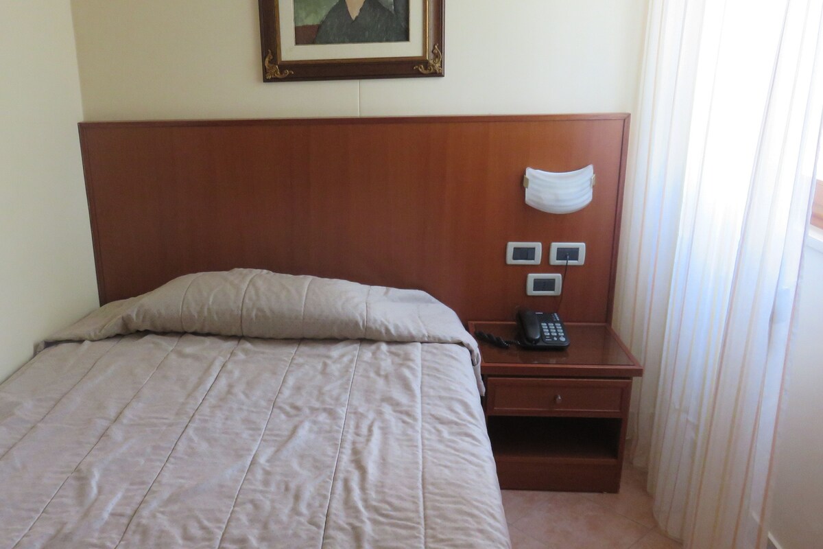 A hotel room with a bed, a nightstand with a phone, and a painting on the wall.