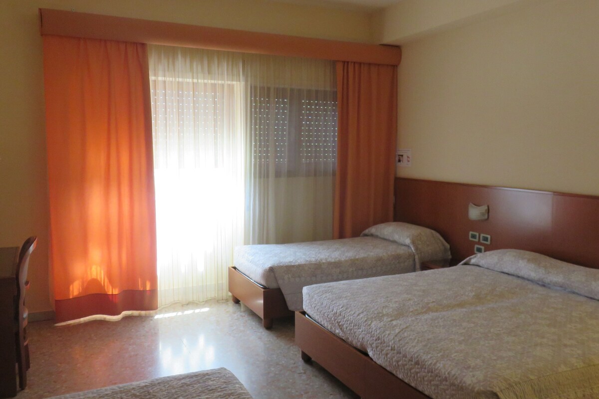 A hotel room with two beds, a desk, and a window with curtains.