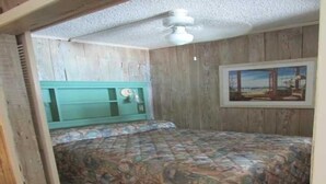 Un dormitorio con cabecera de madera, cama con colcha floral, ventilador de techo y un cuadro en la pared.
