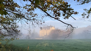 Un castillo en un paisaje brumoso, con un campo verde en primer plano.