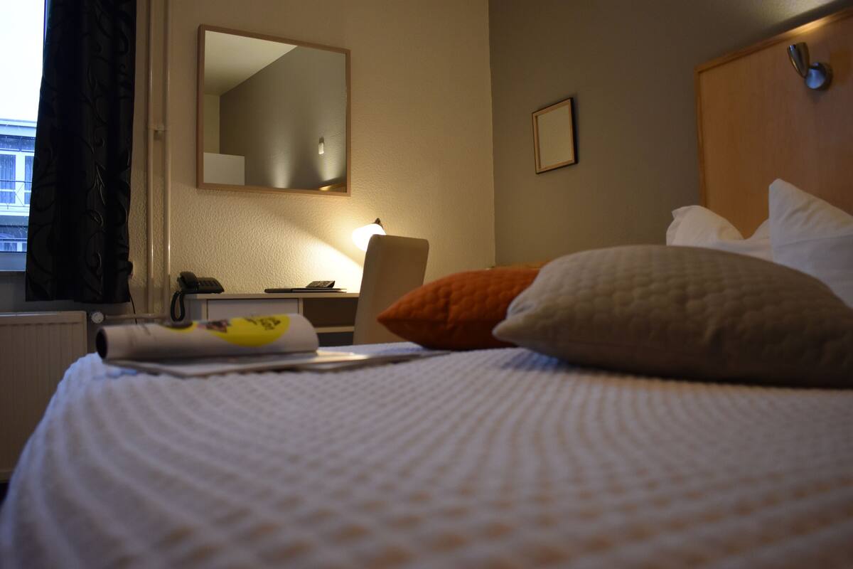 Habitación de hotel con cama, escritorio, silla, lámpara y ventana con cortinas.
