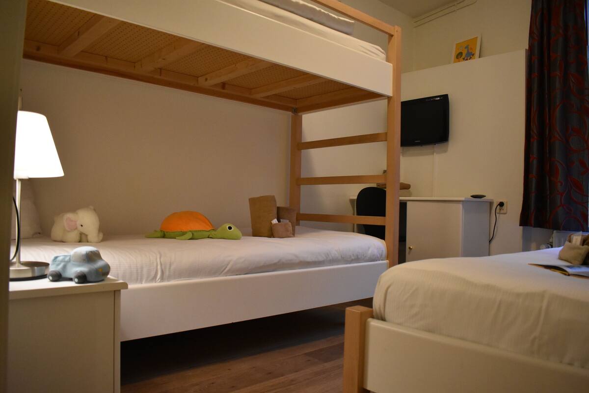 Habitación con literas, un escritorio, una lámpara, un televisor y un mueble pequeño.