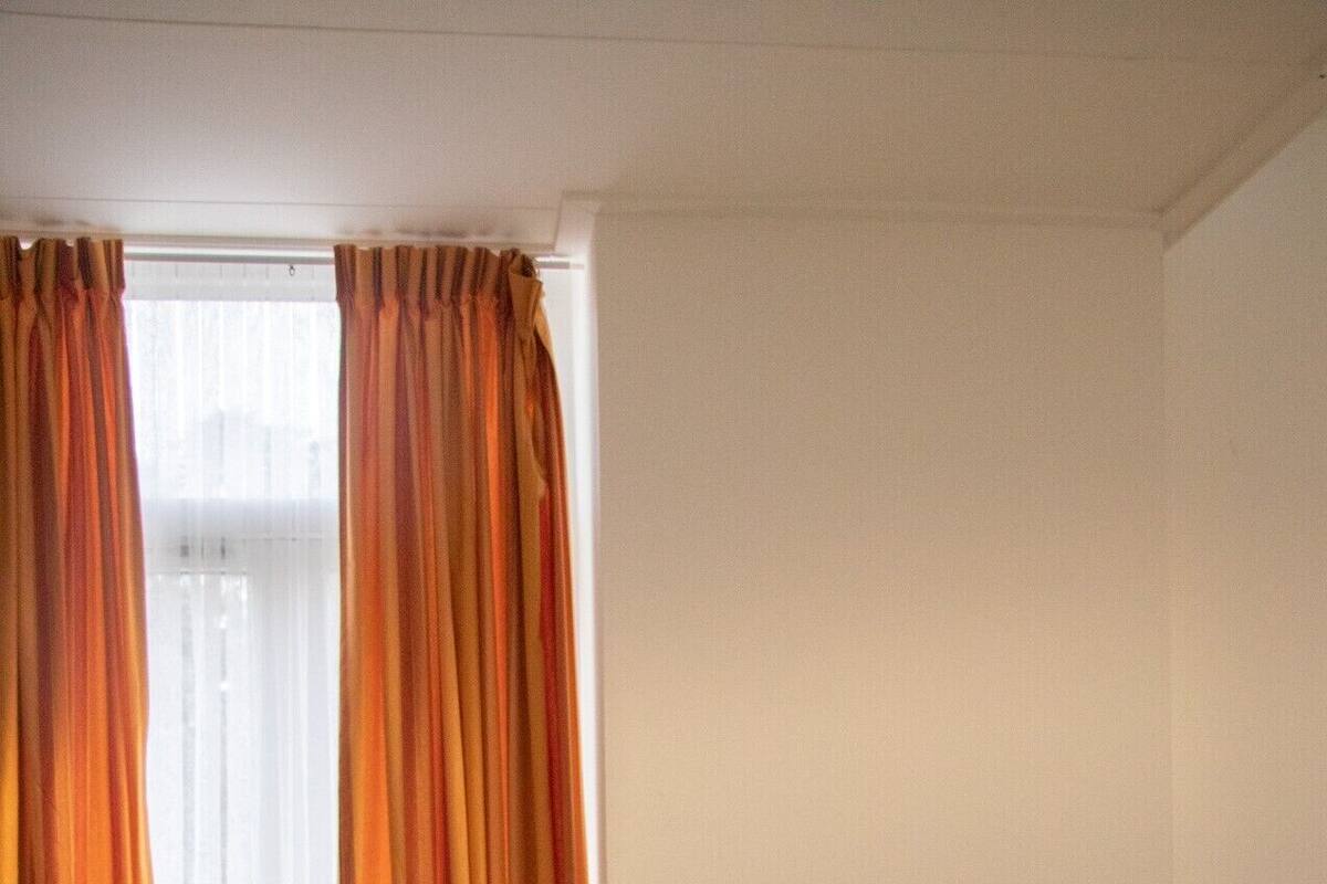 Une chambre d’hôtel avec un lit, du linge de lit blanc et une fenêtre avec des rideaux orange.