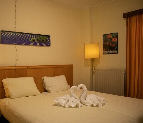 A hotel room with a bed, a painting on the wall, a lamp, and a window with curtains. - Hotel 2000 (Valkenburg aan de Geul)