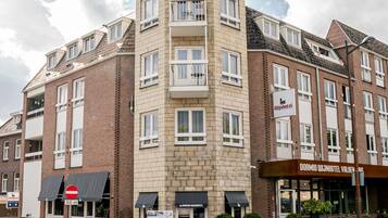 Un hotel de varios pisos con una entrada destacada en esquina, una señal visible para 'DORMIO WILJNHOTEL VALKENBURG' y un cartel de '50m' de prohibido el paso.