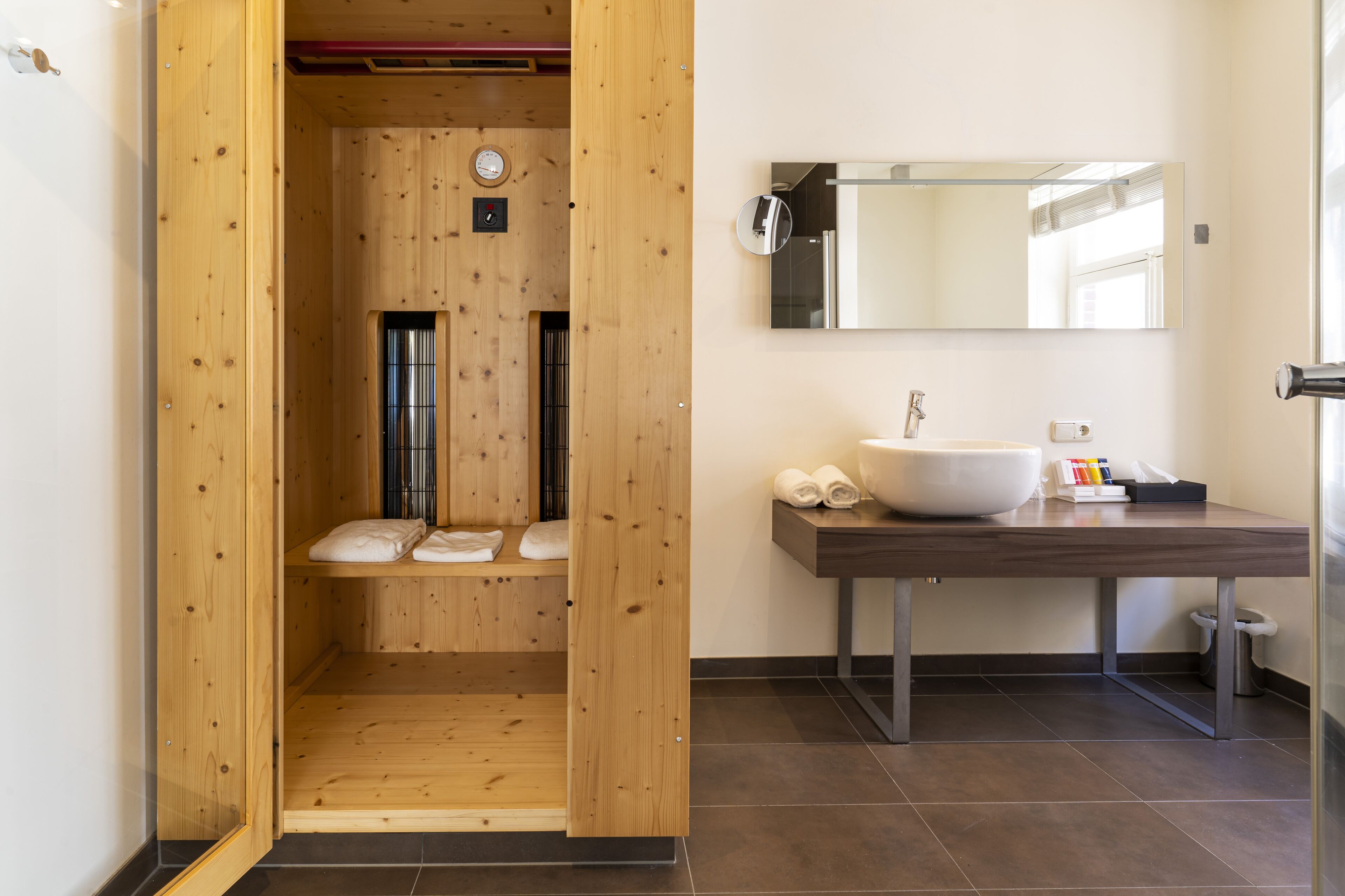 Een moderne badkamer met een houten sauna, een groot wastafel en een spiegel.