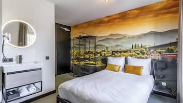 A modern bedroom with a bed, a round mirror, a white sink, and a mural of a landscape.