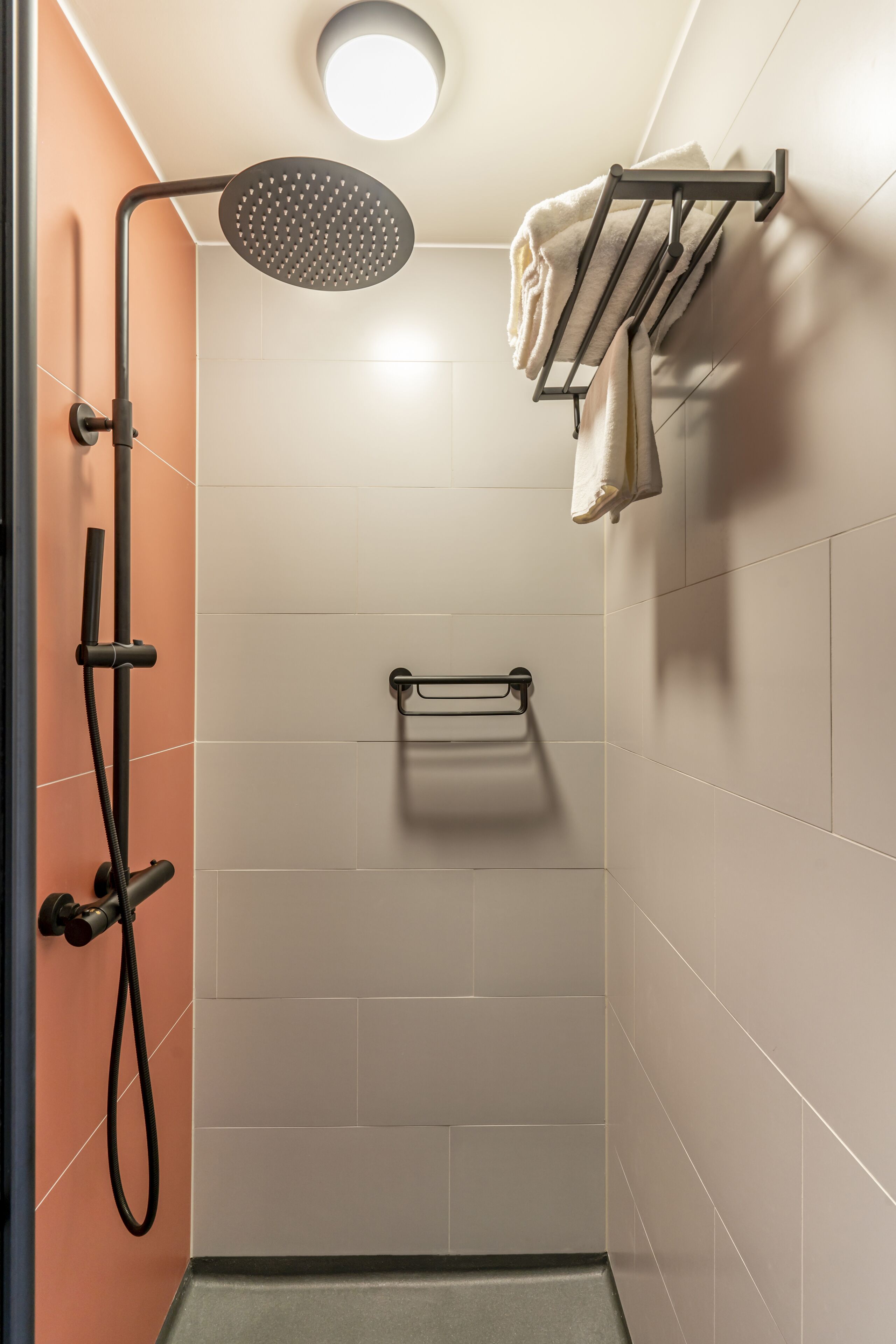 En modern dusch med ett duschmunstycke som kan hållas i handen, en handdukshängare och en handduk som hänger på den.