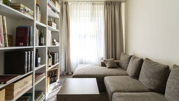 A modern living room with a sofa, a coffee table, and a bookshelf filled with books and wine bottles.