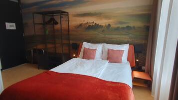 Une chambre d’hôtel avec un lit, une couverture rouge et une fresque représentant un paysage sur le mur.