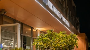 A hotel exterior at night with a sign reading "DORMIO WIJNHOET VALKENBURG". There are outdoor seating areas with tables and chairs, and potted plants in the foreground. - Dormio Wijnhotel Valkenburg (Valkenburg aan de Geul)