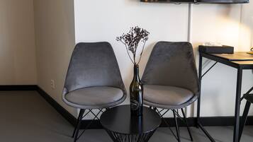 A modern room with two grey chairs, a small table, a vase with flowers, and a flat-screen TV mounted on the wall.