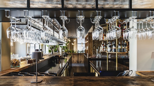 A bar area with multiple hanging wine glasses, shelves with bottles, and a wooden counter. - Dormio Wijnhotel Valkenburg (Valkenburg aan de Geul)