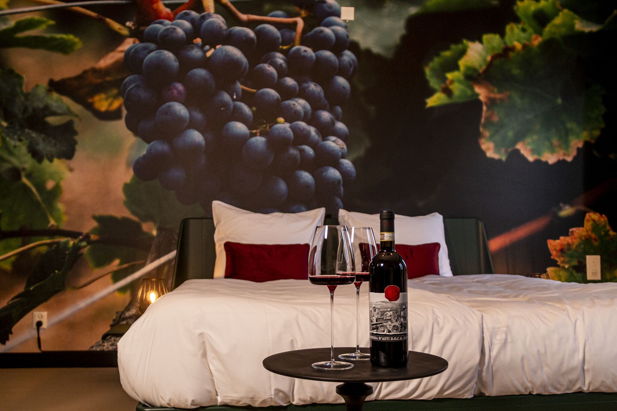 A hotel room with a bed, two wine glasses, and a bottle of wine on a small table.