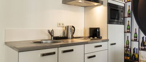 A modern kitchen with a stainless steel sink, kettle, and microwave. There is a wine rack with bottles on the right.