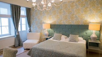 A bedroom with a large bed, two bedside tables with lamps, a tufted headboard, a window with curtains, and a chair.