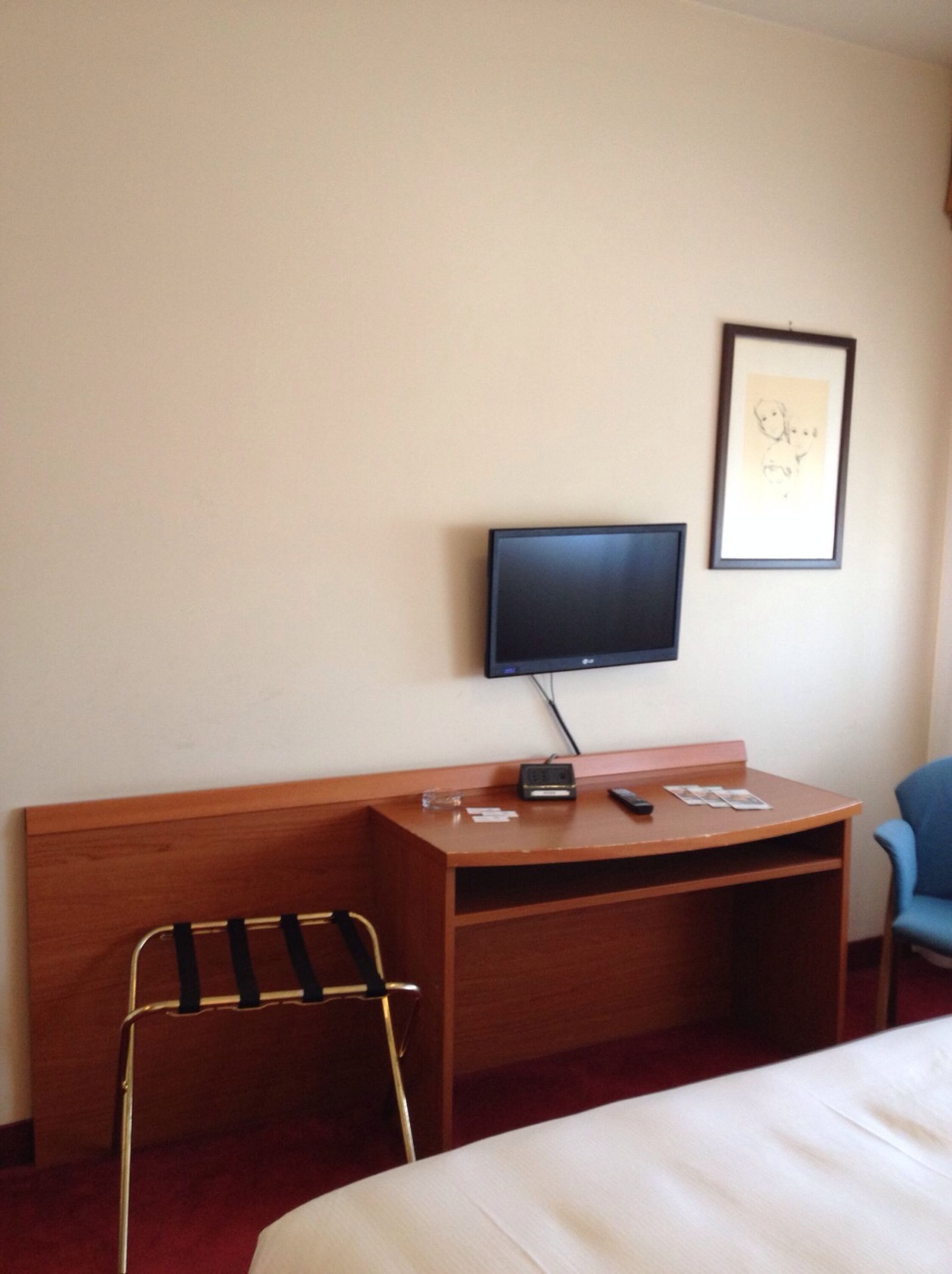 A hotel room with a bed, a desk with a computer, a chair, and a television on the wall.