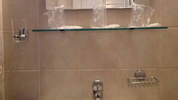 Un baño con lavamanos blanco, un espejo y un estante de vidrio sobre el lavamanos que sostiene una toalla y un vaso.