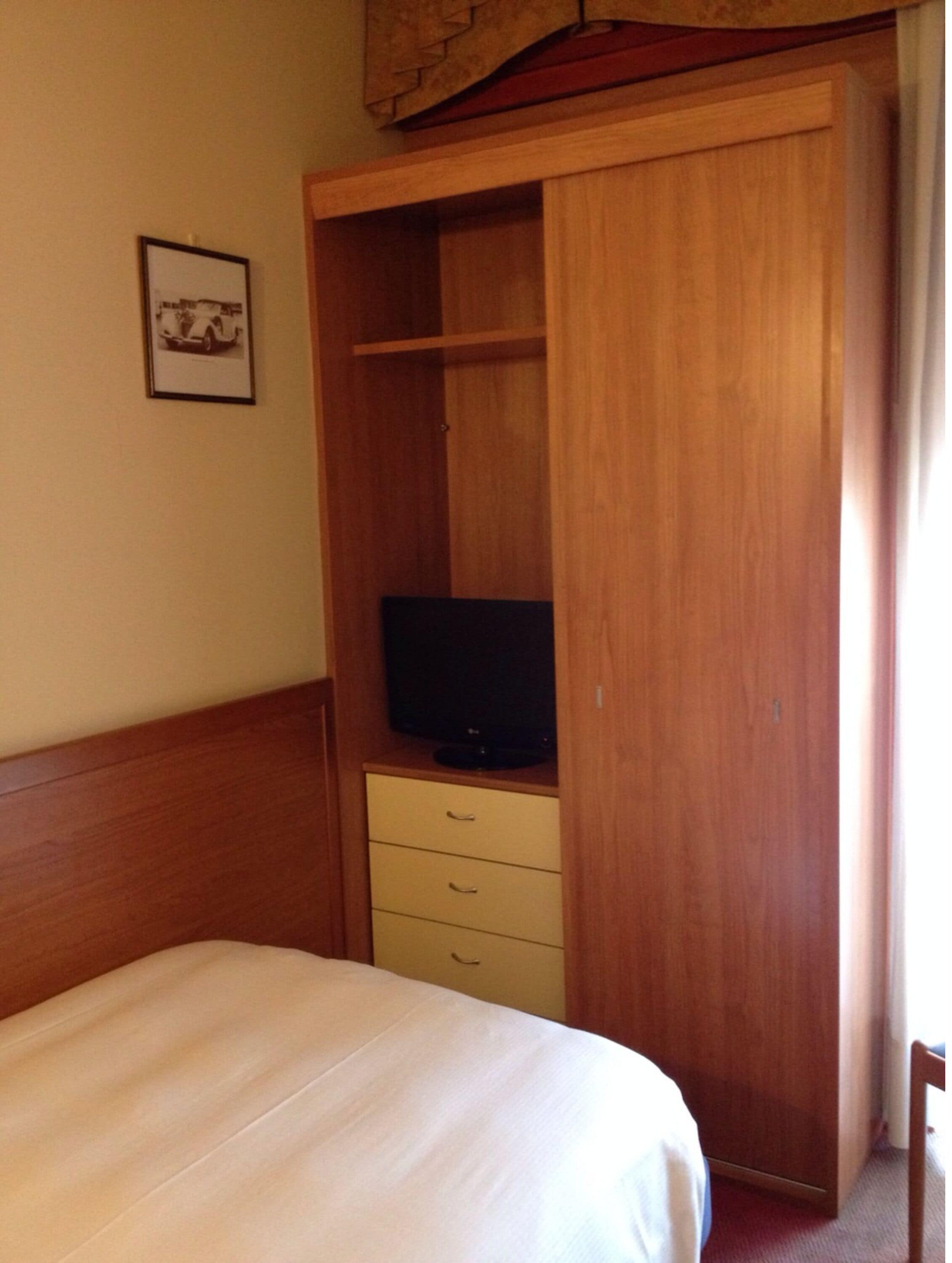 A hotel room with a bed, a wooden wardrobe with a television, and a framed picture on the wall.