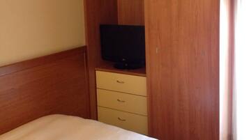 A hotel room with a bed, a wooden wardrobe with a television, and a framed picture on the wall.