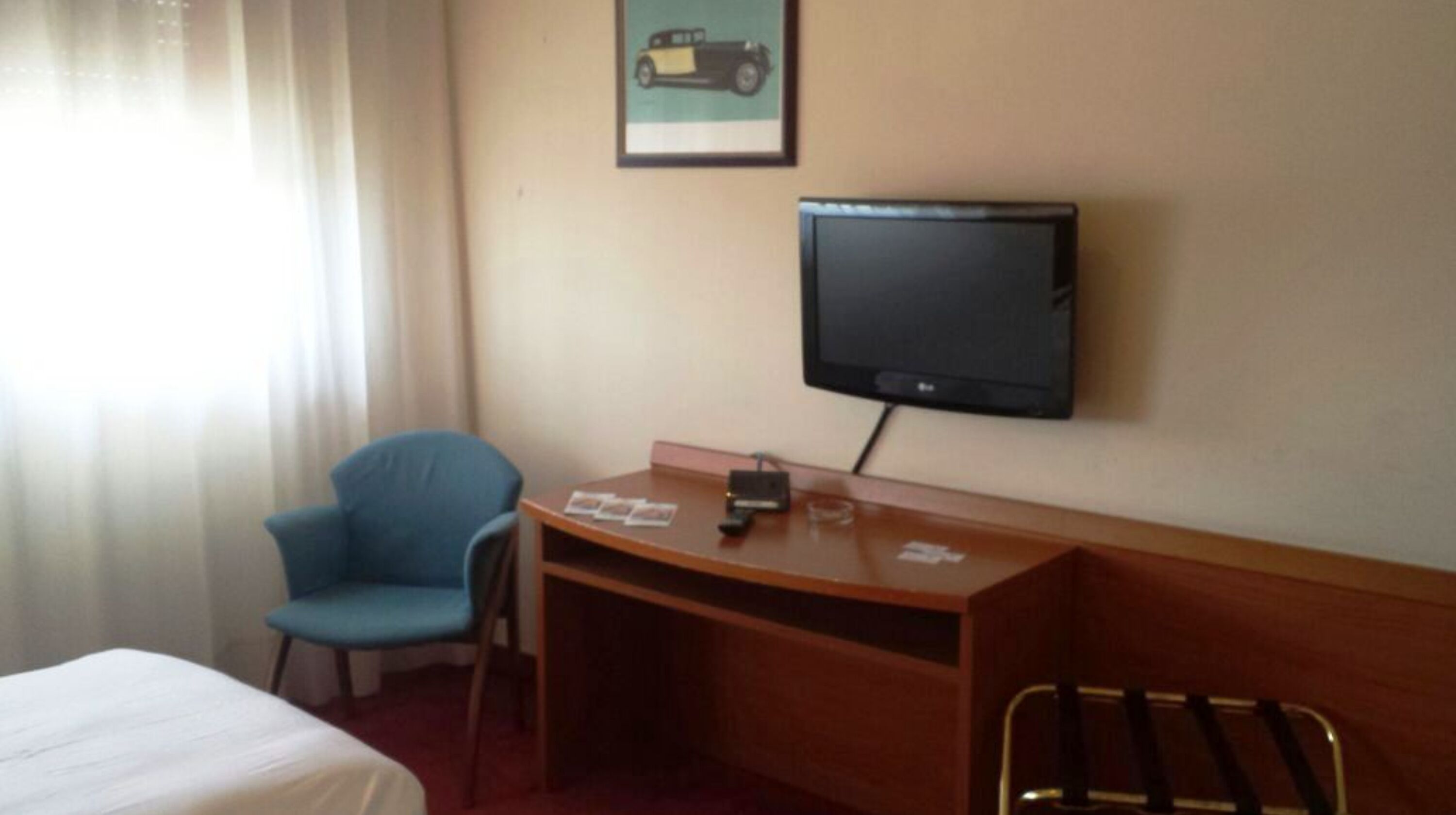 Une chambre d’hôtel avec un lit, un bureau avec une télévision, une chaise et une fenêtre avec des rideaux.