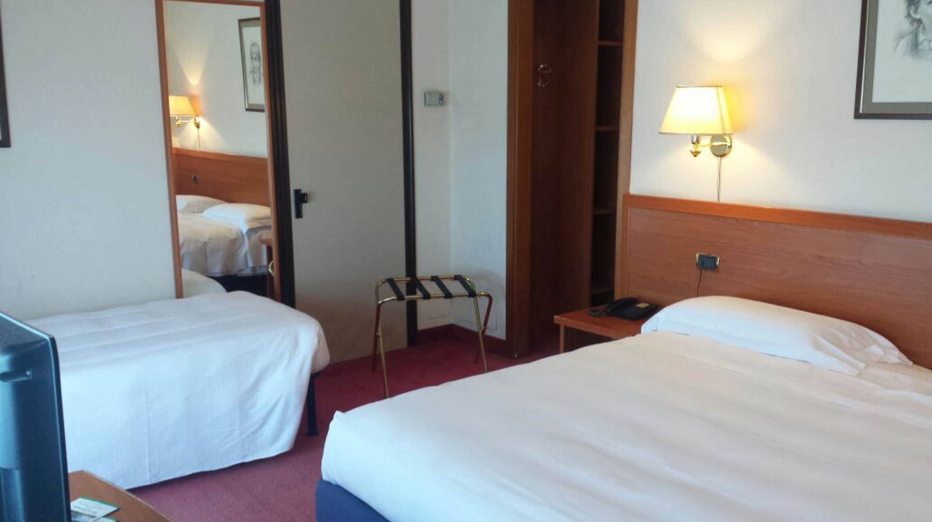 A hotel room with two single beds, a desk with a lamp, a telephone, and a mirror.