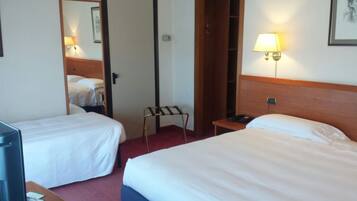 A hotel room with two single beds, a desk with a lamp, a telephone, and a mirror.