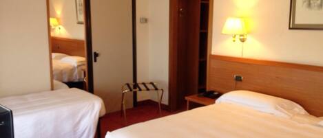 A hotel room with two single beds, a desk with a lamp, and a chair.