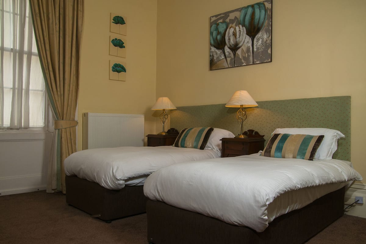 A double bed with two bedside tables, a radiator, and a window with curtains.