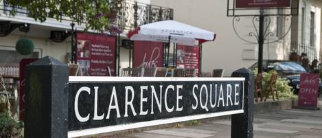 Una señal de calle indica Clarence Square, con un restaurante al fondo.
