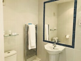 Un baño con un lavamanos blanco, un perchero para toallas, un estante de vidrio con artículos de aseo y un espejo con marco de azulejos azules.