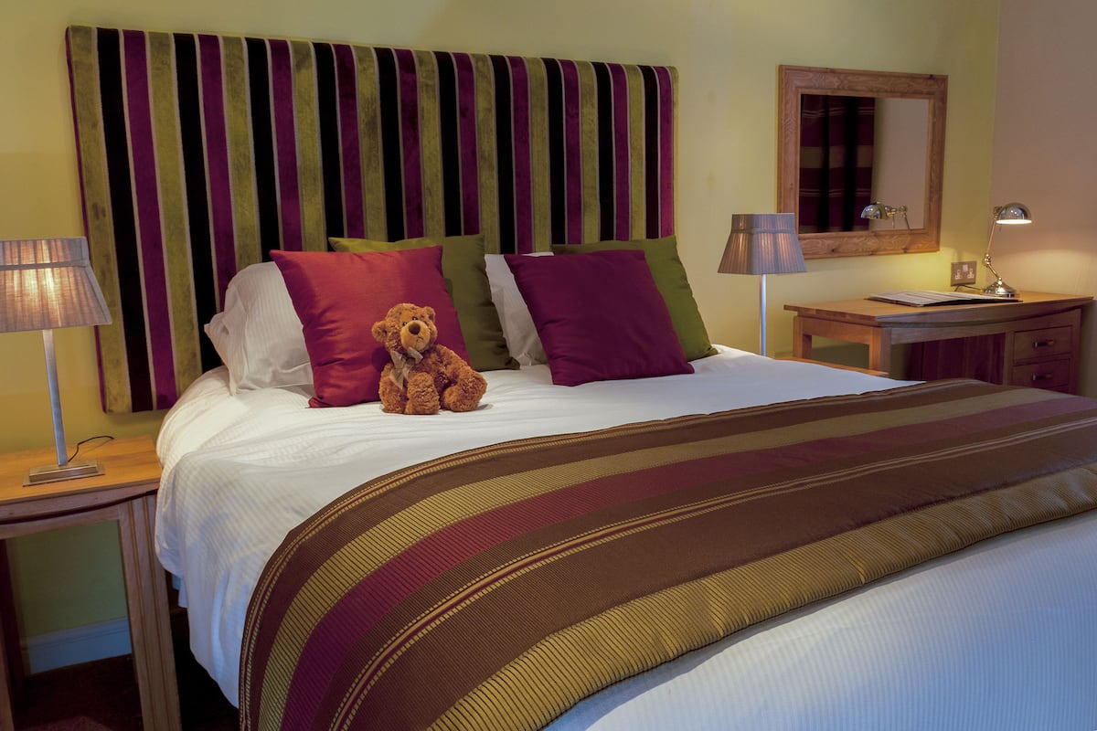 A neatly made bed with striped bedding, a teddy bear, and multiple pillows.