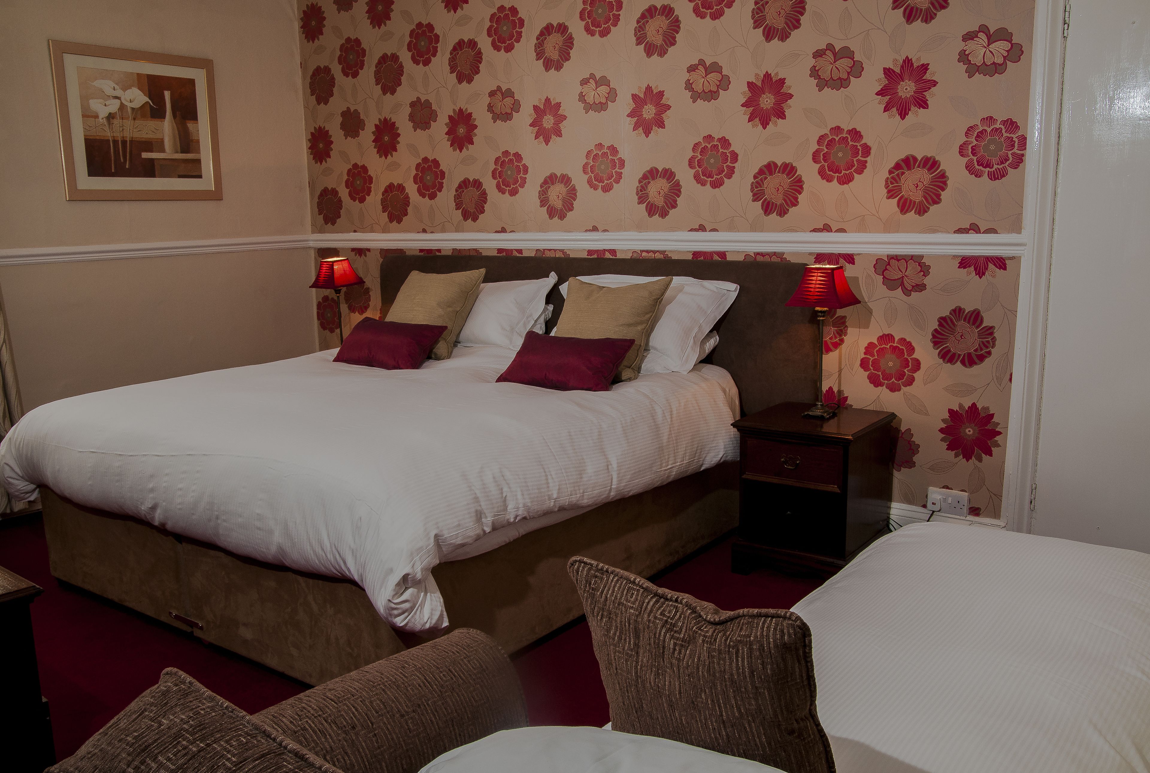A neatly made bed with white and brown bedding, two bedside tables with lamps, and a floral wallpaper pattern on the wall.