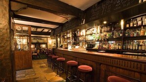 A bar area with stools, a counter, and shelves of bottles. - Crown and Cushion (Chipping Norton)